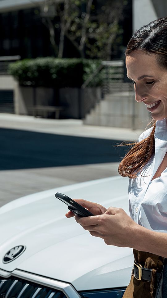mosolygó nő egy skoda modell mellett áll telefonnal